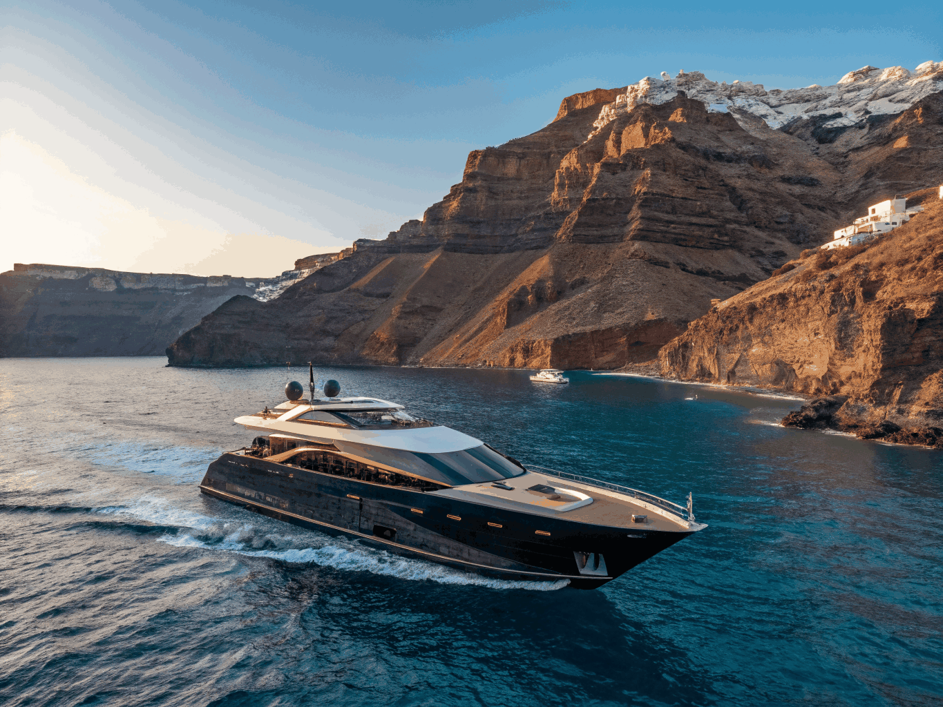 Catamaran navigating the azure Aegean waters along Santorini caldera at sunset