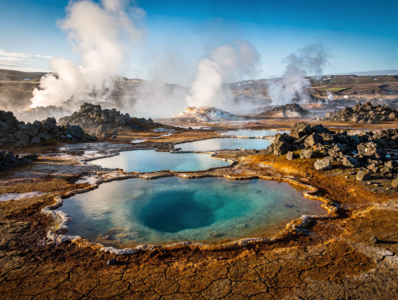 Steam rising from natural geothermal pools framed by volcanic rock